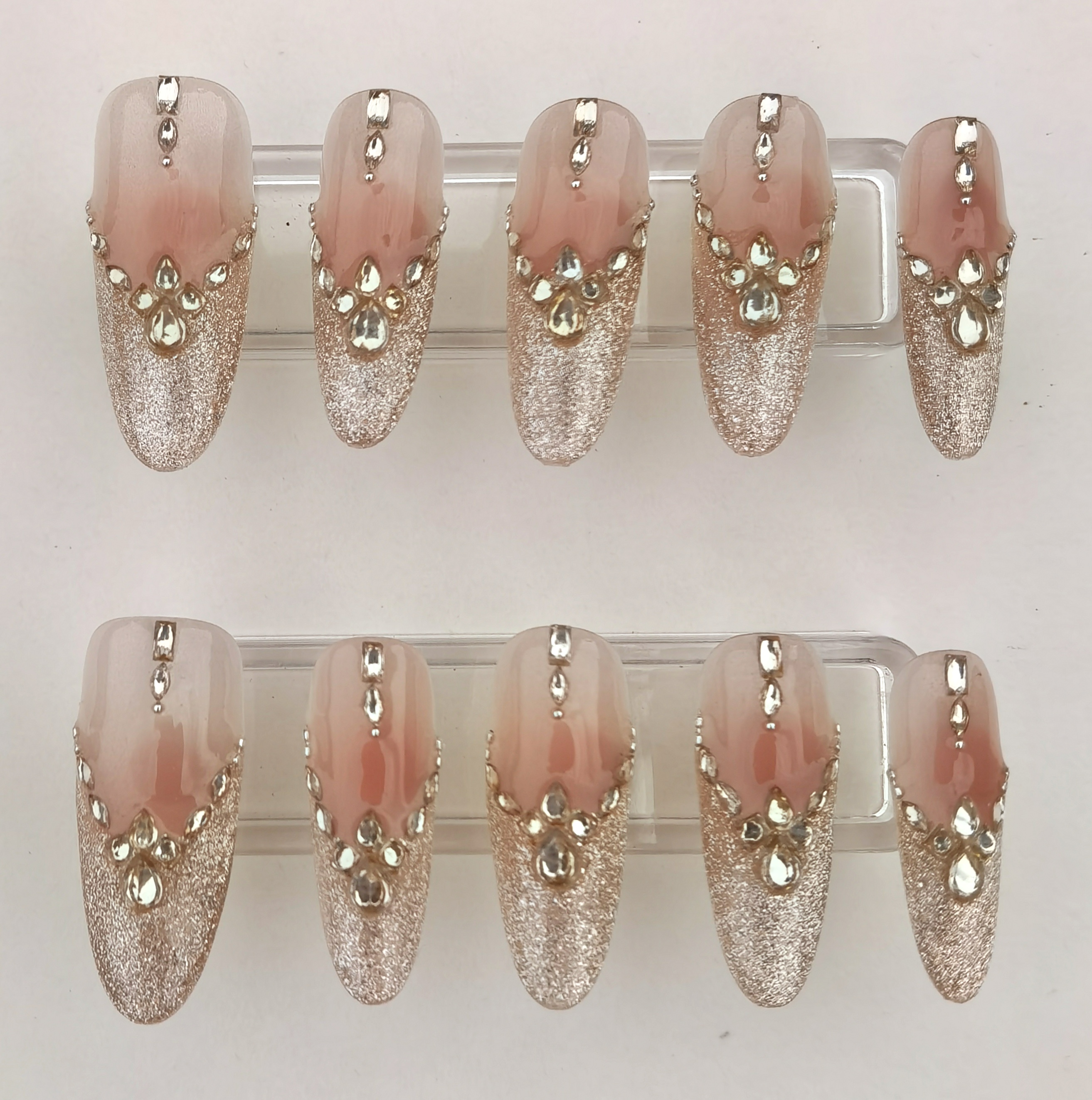 A 24-piece full set of luxurious almond-shaped press-on nails featuring a nude ombre base, rose gold glitter tips, and sparkling 3D rhinestone embellishments.