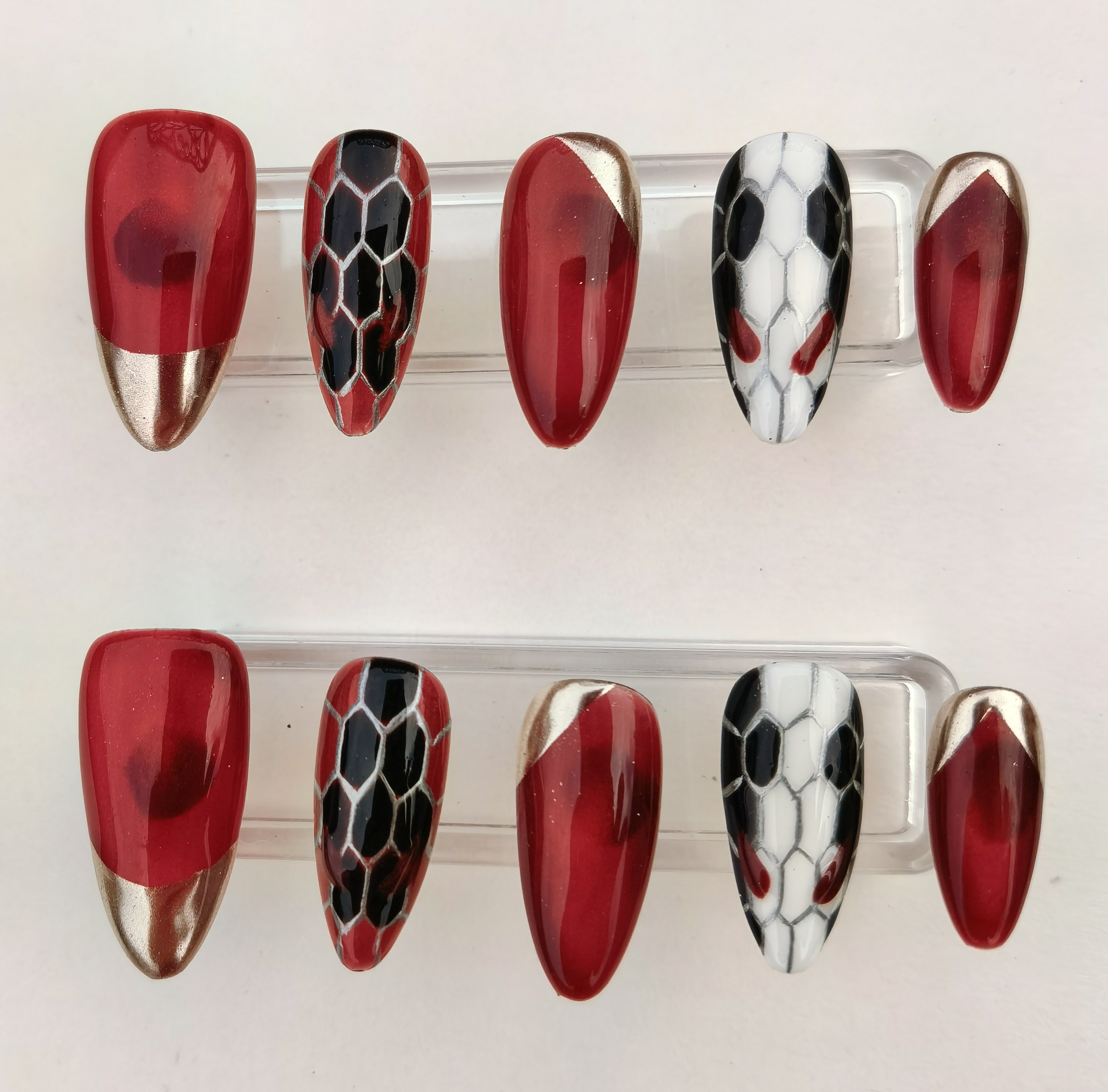 A 24-piece full set of handcrafted press-on nails featuring a luxurious almond shape, medium length, and a glossy finish. The design includes striking red nails with gold chrome tips, alongside bold black and white snake-skin pattern nails with red accents.