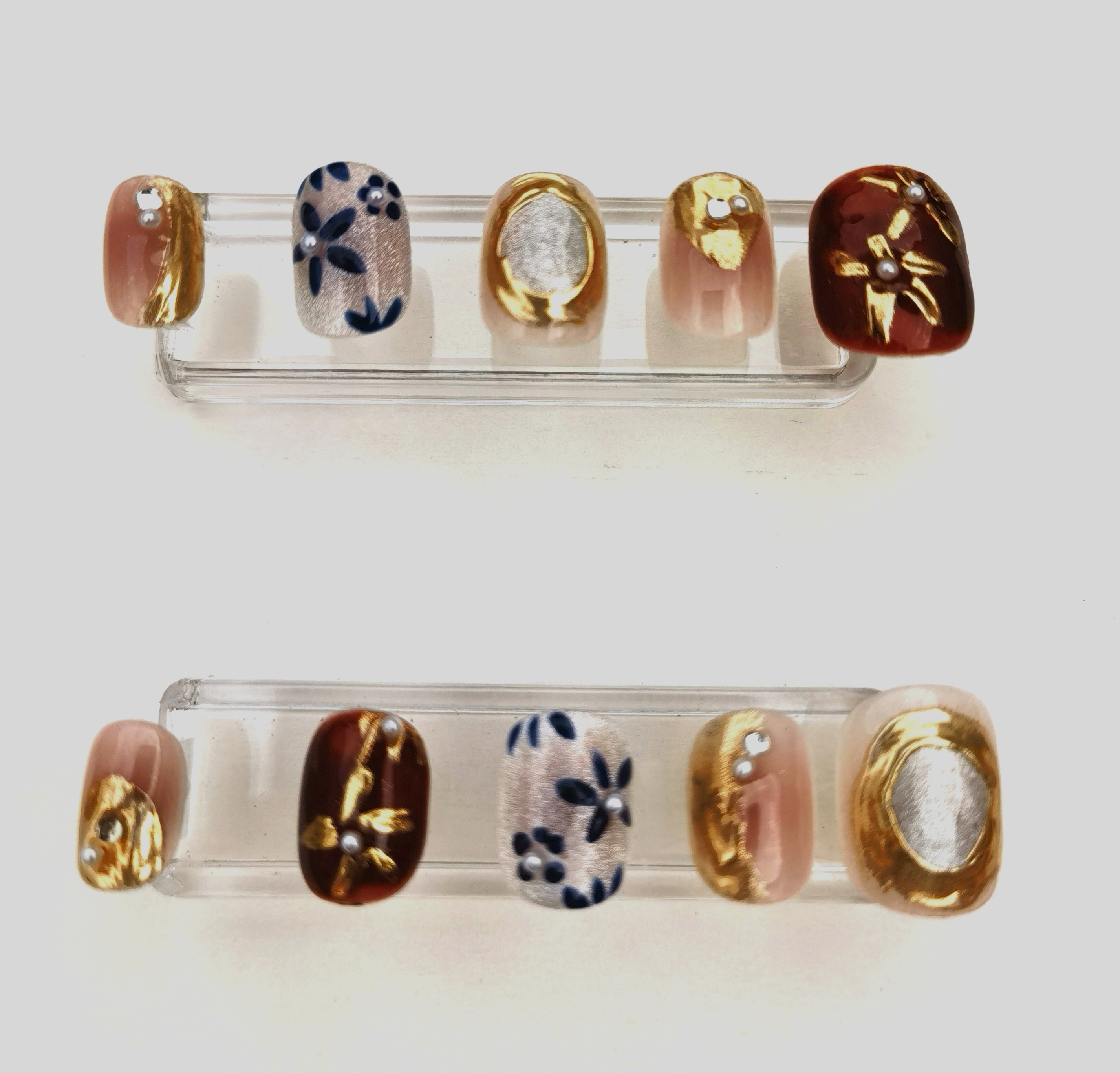 A 24-piece full set of short oval press-on nails featuring a luxurious mix of glossy, cat-eye, and metallic gold finishes with intricate floral patterns and delicate 3D pearl embellishments.