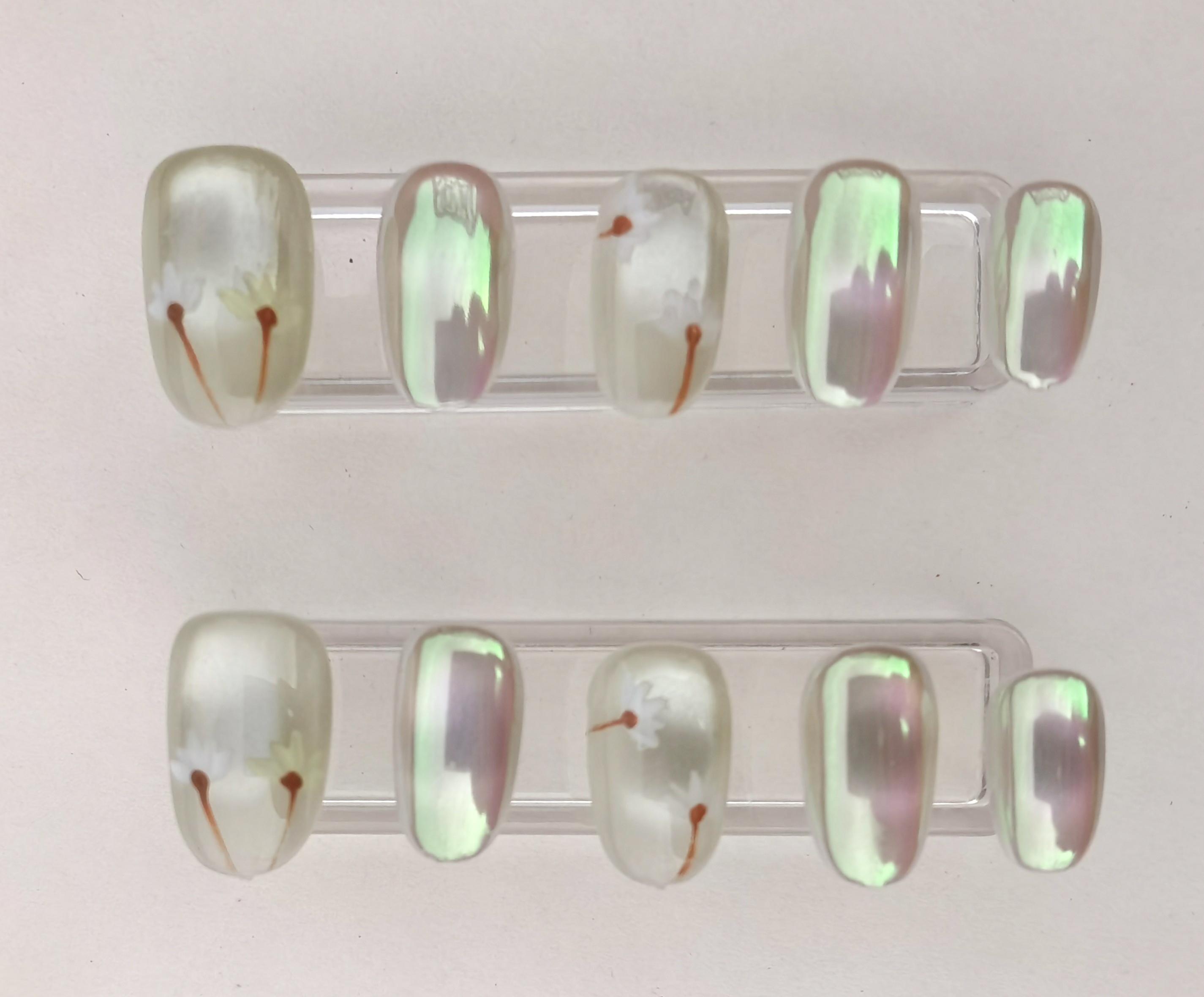 A 24-piece full set of short oval press-on nails featuring a pearlescent shimmer finish and delicate white floral accents.